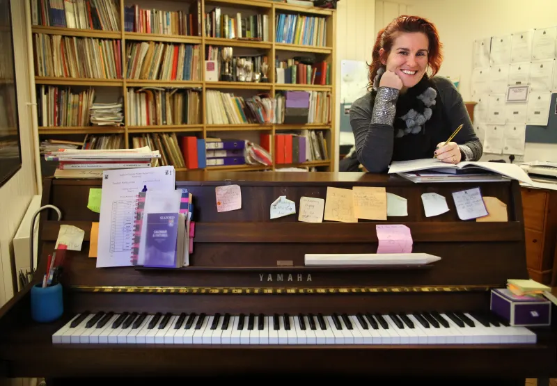 Sara Vernon, smiling, leaning over a Yamaha piano